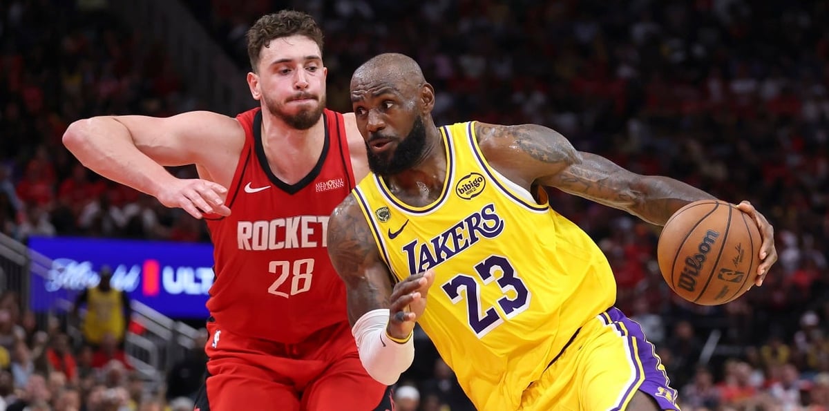 NBA player in Lakers yellow jersey number 23 dribbling basketball while defended by Rockets player in red jersey during game