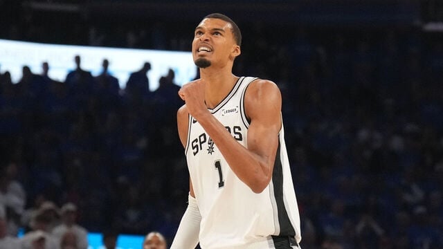 Basketball player wearing white Spurs jersey number 1 looking upward during a game with crowd in background