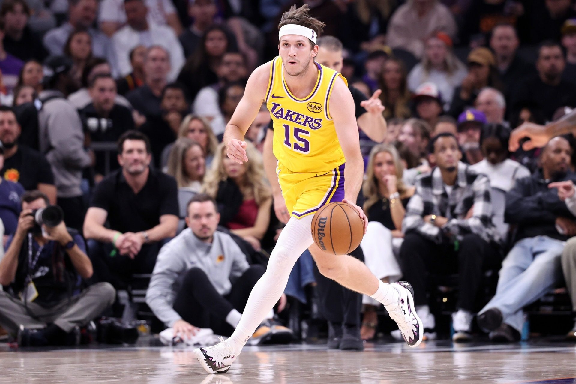 Lakers player number 15 in yellow jersey dribbling basketball during game with crowd in background