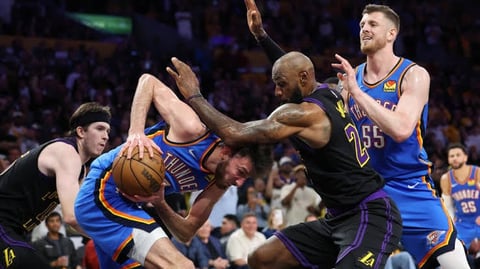 Basketball players in intense game action, with a player in black jersey driving past defenders in blue jerseys during an NBA game.