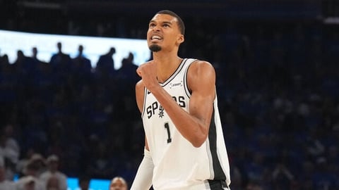 Basketball player wearing white Spurs jersey number 1 standing on court with crowd in background
